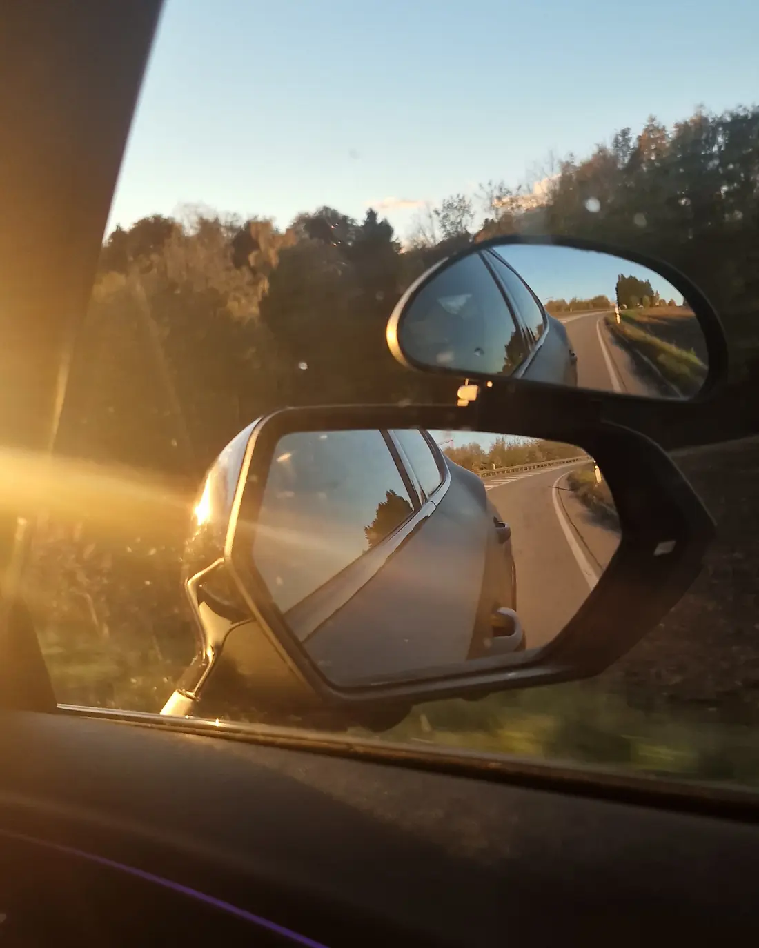 Blick aus dem Fahrschulauto in den Außenspiegel, Abendsonne über einer Landstraße